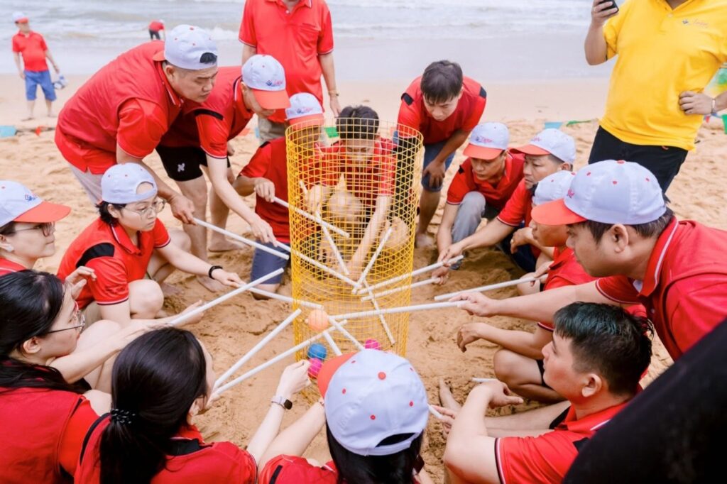 Employees in red shirts and white caps participating in an interactive beach team-building game on the sand.