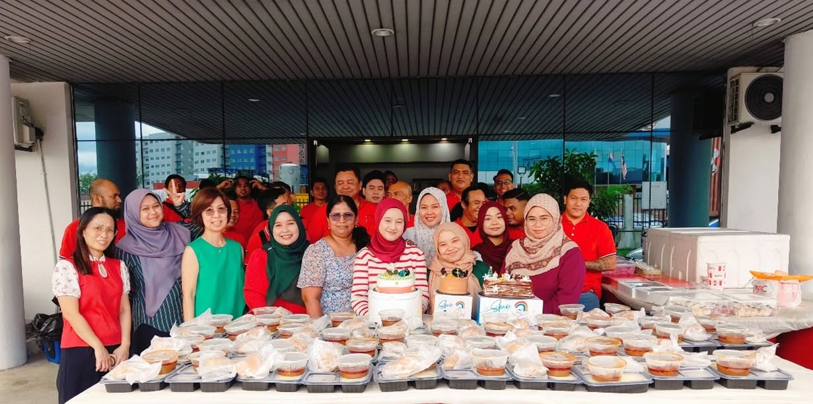 Employees posing outdoors behind a long table arranged with packed meals and Christmas cakes.