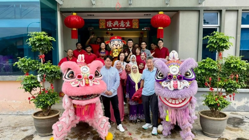 A group photo taken outside an office building featuring a pink and a purple lion dance costume alongside a person dressed as the God of Wealth.