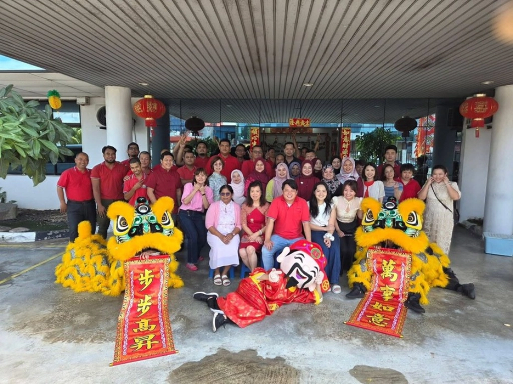 A large group of employees posing outdoors with two yellow lion dance costumes and a person dressed as the God of Wealth.