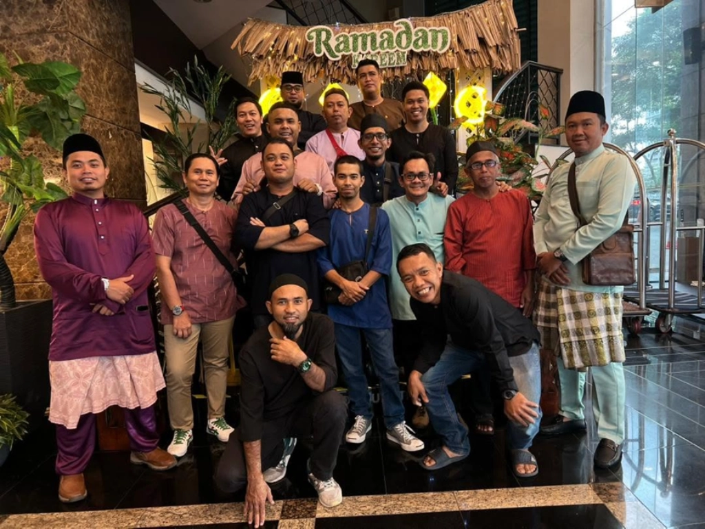 A group of twelve men posing on a staircase in front of the same "Ramadan Kareem" display, dressed casually in traditional and modern attire.