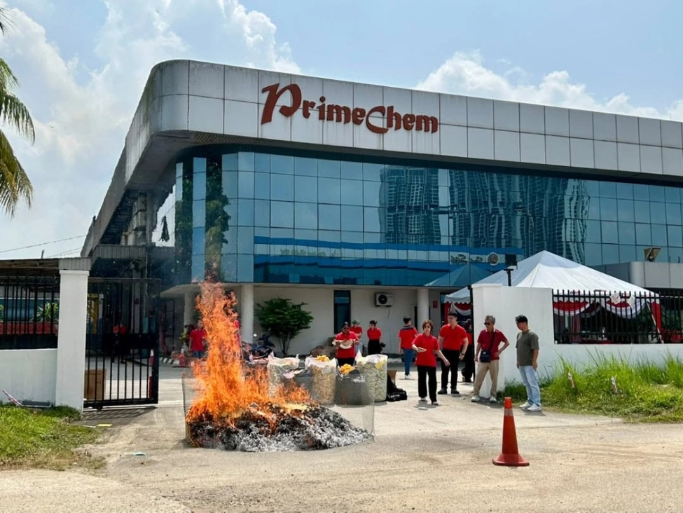 Employees standing near a large blazing fire pit with joss paper burning outside the PrimeChem building.