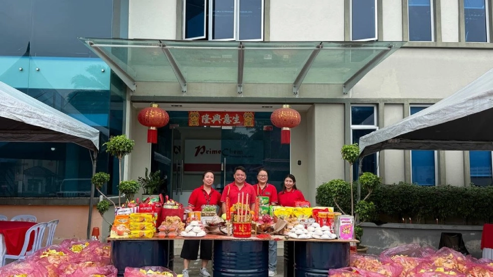 Four employees posing in front of the PrimeChem entrance decorated with red lanterns and offering tables.