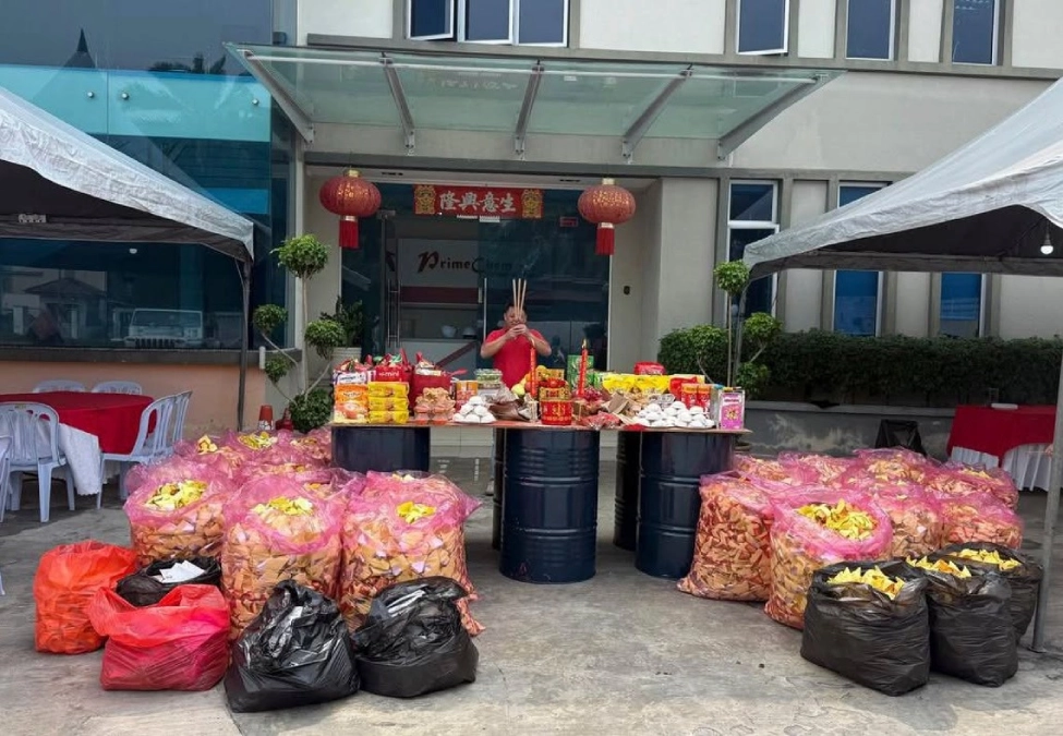 Extensive display of food offerings and large bags of joss paper set up in front of the PrimeChem entrance.