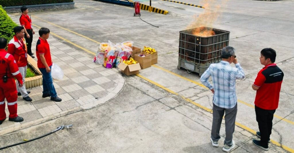 A small group of Riverbank Vietnam employees standing outdoors burning joss paper and colorful paper offerings in a metal cage as part of the Hungry Ghost Festival customs.