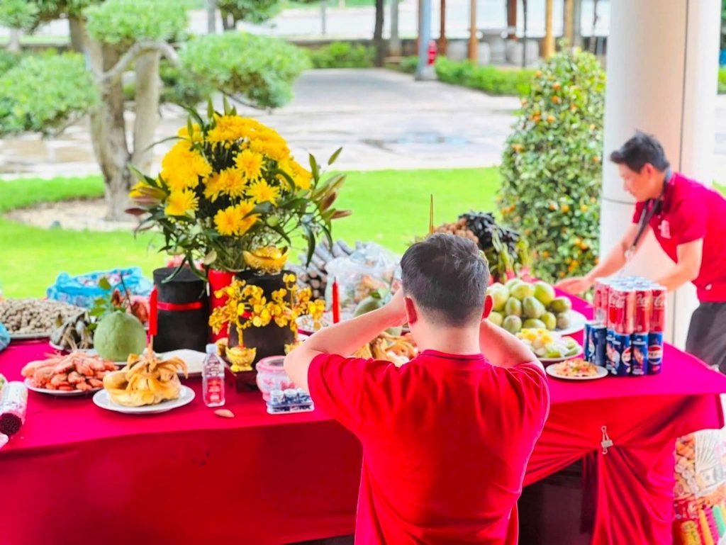 Employee praying with hands folded in front of a ceremonial offering table at Riverbank Vietnam.