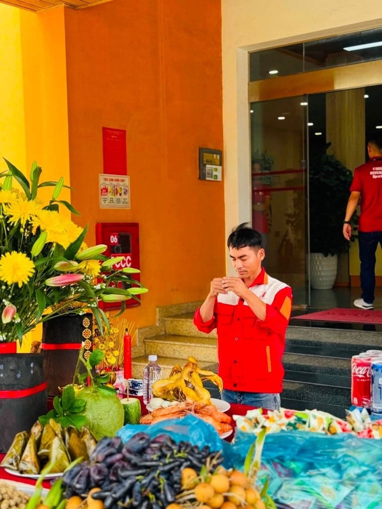 Employee holding incense during a prayer ritual next to a vibrant table of offerings at Riverbank Vietnam.